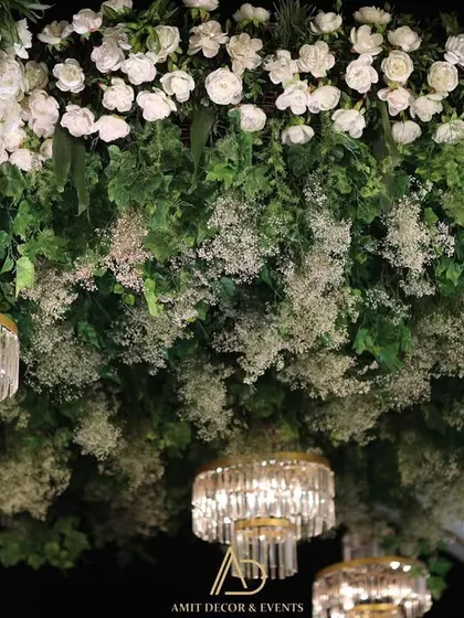 A close-up of the ceiling decor, showing mini crystal chandeliers nestled within a dense canopy of white flowers and fresh greenery.