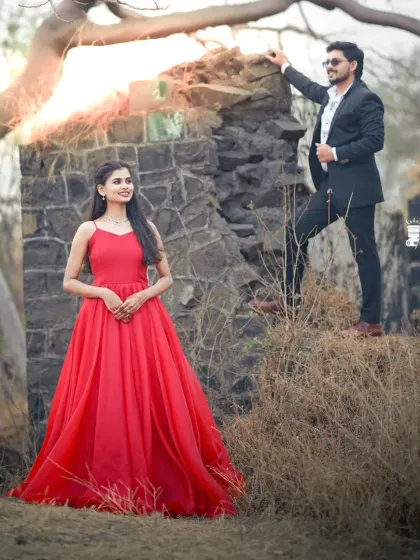 A classic pre-wedding shot in a rustic setting. The bride's simple red ball gown provides a beautiful pop of color against the natural landscape.