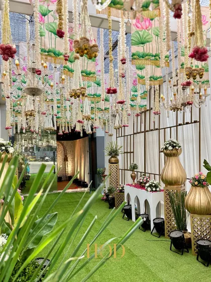 A view from inside the green-carpeted aisle, looking back towards the entrance. The ceiling is adorned with hanging lotus-printed fabric panels and floral tassels, creating a unique and artistic look.
