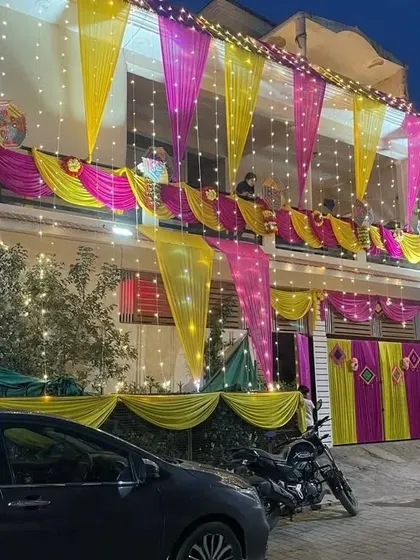 A house decorated for a night function, with yellow and pink drapes on the balcony and gate, all lit up with fairy lights.