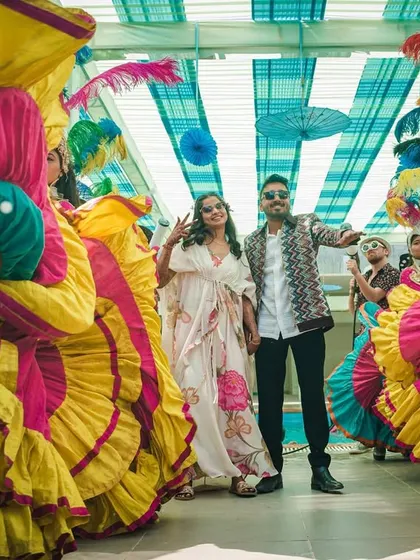 A beautiful shot of the couple during their pool party entry. They are framed by dancers in vibrant carnival costumes, creating a stunning photo opportunity.