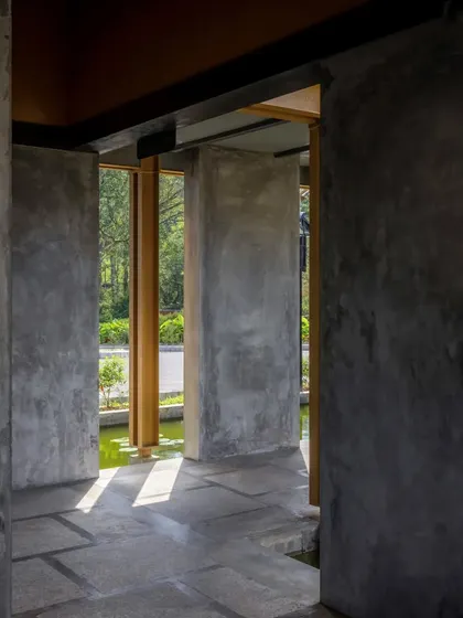 The use of raw concrete walls and stone flooring creates a cool, shaded corridor that opens up to views of the water channel and greenery, blurring the line between inside and out.