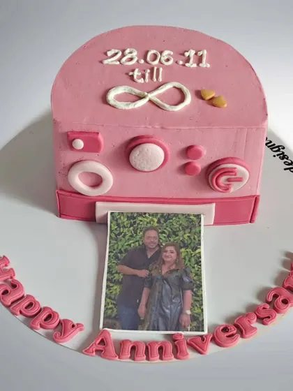 An anniversary cake designed as a pink Polaroid camera. The photo that slides out features a picture of the couple, making it a sweet and interactive gift.