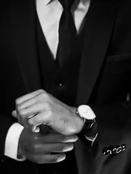 A classic black and white shot focusing on the groom's accessories. The crisp details of the suit cuff, the elegant watch, and the confident posture all contribute to a timeless portrait of the groom.