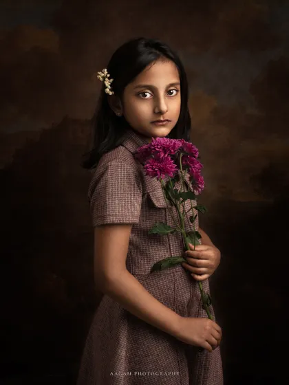 A beautiful, classic portrait of a young girl holding flowers. The dark, painterly background and her serene expression give this image a timeless, old-world feel.