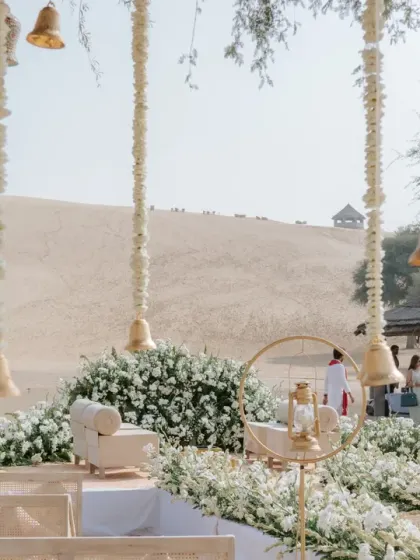 A detailed view of the sand dune wedding mandap, featuring hanging bells and floral garlands against the desert backdrop.