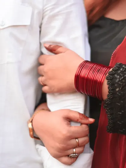 A detail shot of the bride's hands, adorned with red bangles, holding her husband's arm. A simple yet powerful image of togetherness.