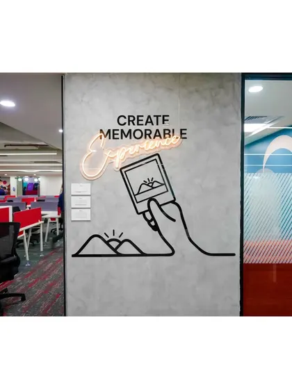 A neon sign with the words "Create Memorable Experiences" serves as an inspiring focal point in this common area. The simple line art on the concrete-finish wall adds a touch of modern, industrial chic.