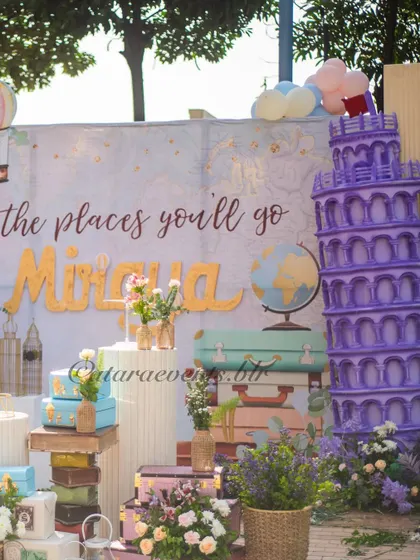 A detailed shot of the "Around the World" party decor, featuring a stack of vintage-style suitcases, a globe, and the Leaning Tower of Pisa, all in a beautiful pastel color palette.