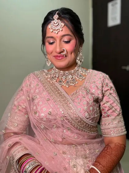 A beautiful bride in a pastel pink lehenga. This is a raw, no-filter shot showing the final touches, with a focus on blushed cheeks and shimmery eyes.