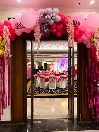 A glamorous and grand entrance arch for a Barbie-themed party, using various shades of pink, gold, and silver balloons with floral and fringe details.