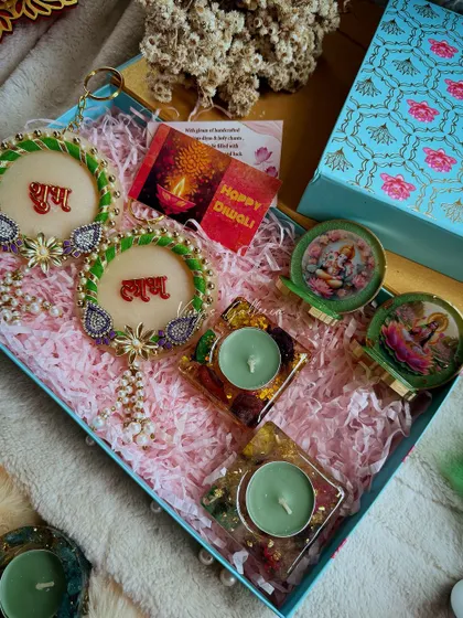 A green and gold Diwali hamper with "Shubh Labh" hangings, square tealight holders, and mini deity stands.