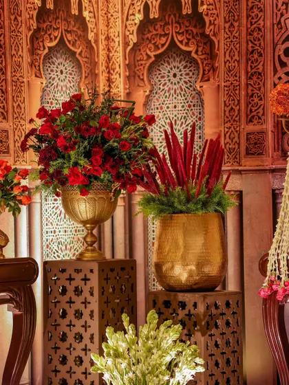 A corner vignette featuring floral arrangements on illuminated pedestals with geometric cutouts. The backdrop of carved arches adds another layer of texture and historical reference.