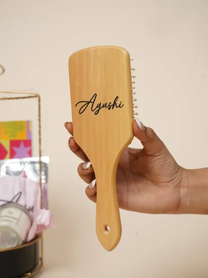 A wooden hairbrush, custom-engraved with the recipient's name, adds a touch of personalized luxury to her birthday hamper.