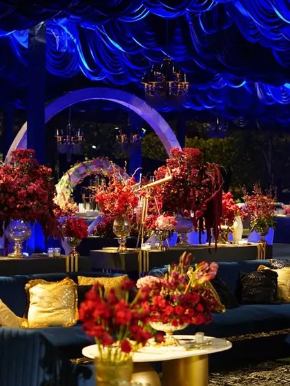 The lounge area was a study in contrasts, with plush blue velvet sofas, sequined cushions, and vibrant red floral arrangements creating a dramatic and warm space.