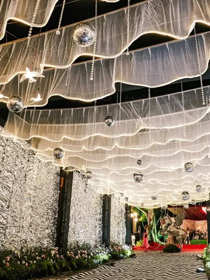 A grand entrance tunnel for a reception, featuring shimmering silver foil walls and a ceiling of draped fabric with hanging disco balls.