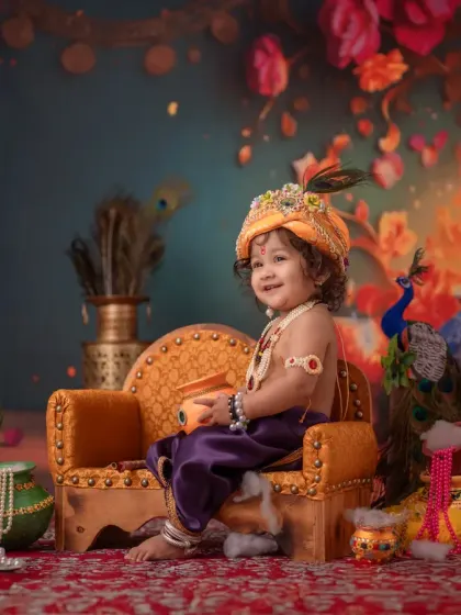 A joyful portrait of a baby dressed as Lord Krishna, smiling brightly in a festive setting. The warm lighting and colorful decor create a truly magical atmosphere for this kids cultural photoshoot.