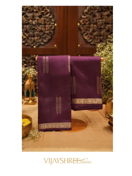 A rich purple Kanjivaram with mango borders and traditional motifs, hung to display its full beauty.