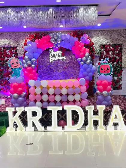 Another look at a grand Cocomelon first birthday stage. This angle shows the full setup with the flower wall, balloon arch, and large illuminated letters.