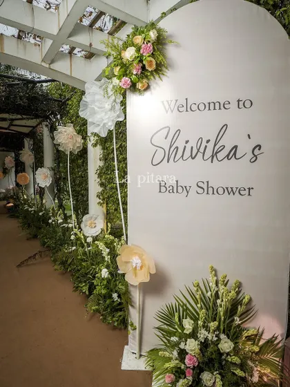 The personalized welcome sign for Shivika's baby shower, elegantly designed and flanked by paper flowers and floral arrangements, ensuring every detail felt special and curated.