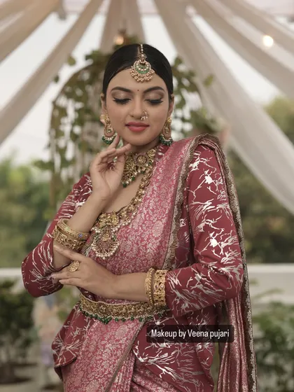 A soft and regal look. The makeup features a subtle smoky eye and a neutral pink lip, allowing the intricate details of the maroon saree and temple jewelry to shine.