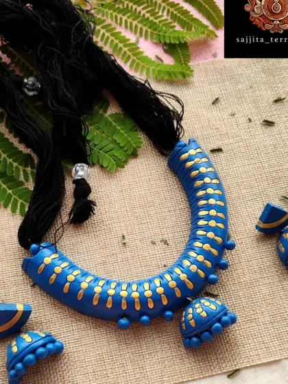 A beautiful 'hansli' shaped necklace in blue and gold. The set comes with matching half-circular jhumka earrings, offering a complete and elegant look.