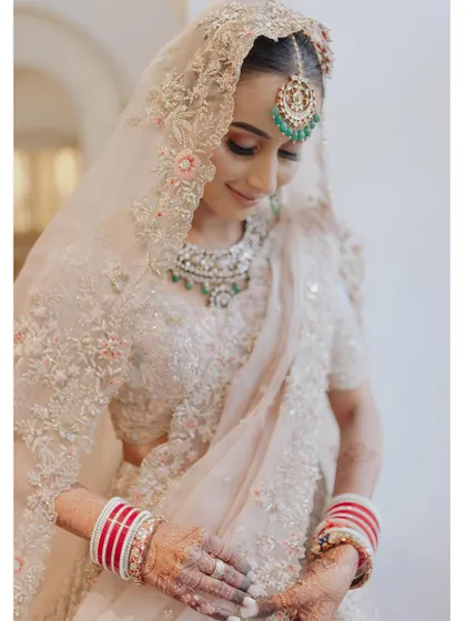 A close-up of the bride in her pastel wedding lehenga, her gentle smile and traditional jewelry creating a soft and beautiful portrait.