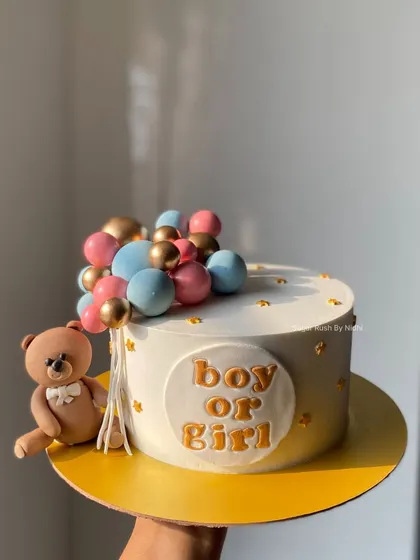 A simple and elegant "Boy or Girl" baby shower cake. This design features a cute teddy bear holding a string of pink, blue, and gold balloons.