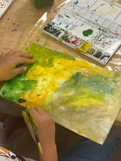 A child experimenting with different shades of green and yellow. Our sessions are a safe space to explore color mixing and see what happens when different hues come together.