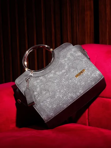 A luxury handbag with a unique floral texture and a metallic ring handle, placed on a rich, red velvet couch. This setting screams opulence and positions the product as a high-end statement piece.