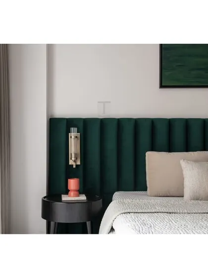 A close-up of the emerald green headboard, showcasing the plush fabric and precise channel tufting. The wall-mounted light fixture is perfectly placed to create a cozy reading nook.