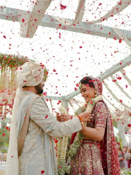 The magical varmala moment, where the couple exchanges garlands under a shower of red rose petals. The floral mandap in the background adds to the romance of this key ritual.