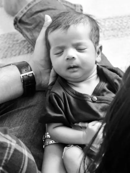 A candid black and white shot from above, showing parents looking down at their sleeping newborn resting peacefully in their lap, a perfect slice of life moment.