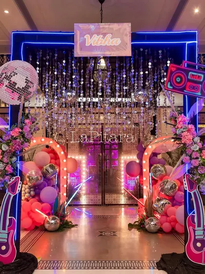 The main entrance to the disco party, framed in blue neon and featuring a shimmering curtain, prop guitars, and a disco ball.