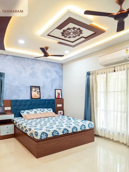 A luxurious master bedroom in our Tambaram villa project, featuring a blue textured accent wall, a custom bed with a cushioned headboard, and an ornate false ceiling design.