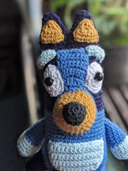 The Bluey doll pictured in front of a window, with natural light highlighting the yarn texture.