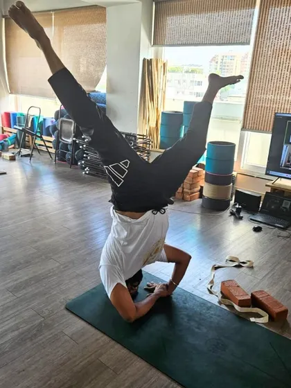 Our TTC program integrates both in-person and online learning. Here, a student practices a variation of Sirsasana (Headstand), demonstrating the dedication of our global community of trainees.