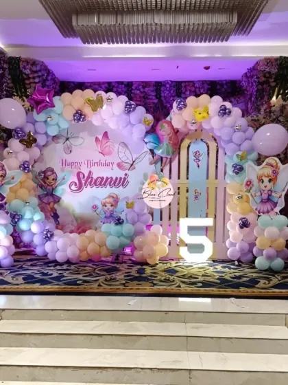 We created this enchanting fairy garden for a 5th birthday celebration. The stage decoration includes a custom backdrop with fairy illustrations, pastel balloon arrangements, and a large light-up number '5'.