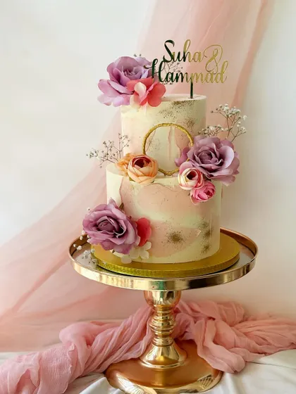 Another view of this romantic two-tier engagement cake, showcasing the beautiful floral arrangement and personalized gold topper on a gold pedestal stand.