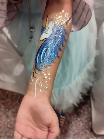 A beautiful unicorn face painting design with glitter, a popular entertainment add-on for kids' parties.