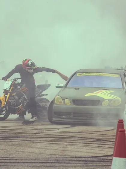 The same burnout shot from a different angle, capturing the raw energy and the partnership between car and bike performers.