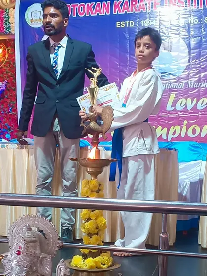 A blue belt student standing with his coach after receiving his award at the state-level championship. The bond between a coach and student is crucial for success.