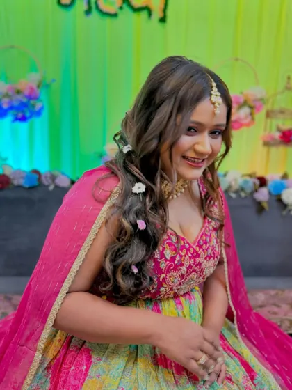 A happy Mehendi bride. Her hair is styled in soft waves with floral accents, and her makeup is a perfect balance of color and glow.