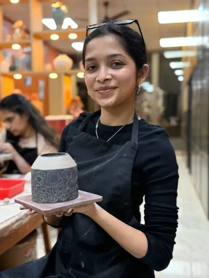 A student proudly shows off her finished sgraffito vase, featuring an intricate, hand-carved mandala pattern. In our classes, you will learn detailed decoration techniques to make your pottery truly one of a kind.