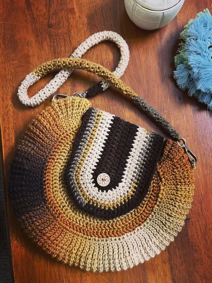 The finished round crossbody bag, featuring a flap closure with a button. The color changes in the yarn make each bag one of a kind.
