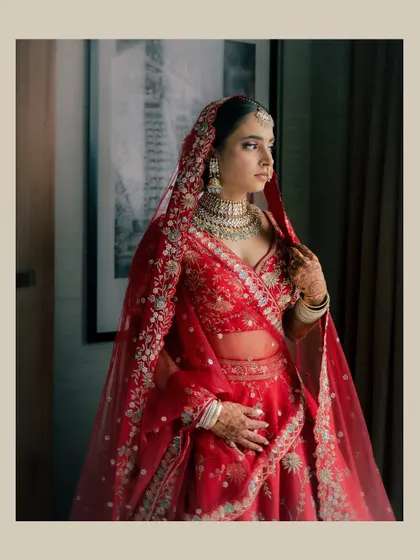 A stunning portrait of Vidushi in her red wedding lehenga. The sheer dupatta and intricate embroidery are complemented by her classic, radiant makeup.