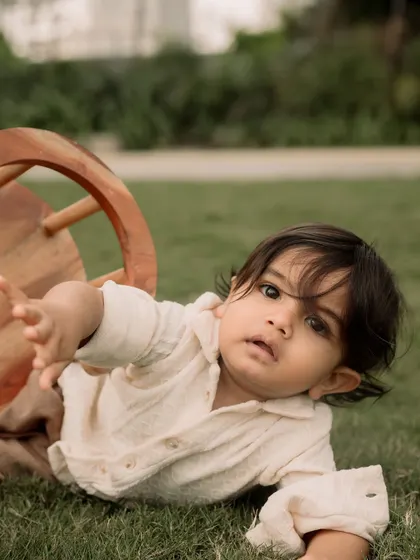 A playful moment captured as a toddler tumbles on the grass, reaching out to the camera.