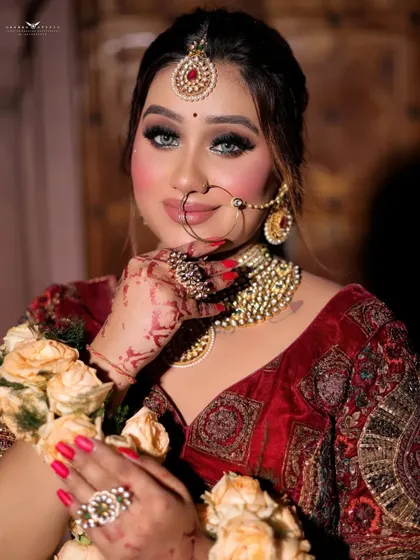 A playful and engaging portrait of a bride. She holds a bouquet of roses, and her pose highlights the intricate henna design on her hand and her stunning bridal nath.
