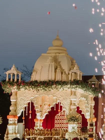 A temple-style mandap glows against the twilight sky, with fireworks adding to the celebratory magic. This image captures the grandeur of a traditional outdoor wedding.