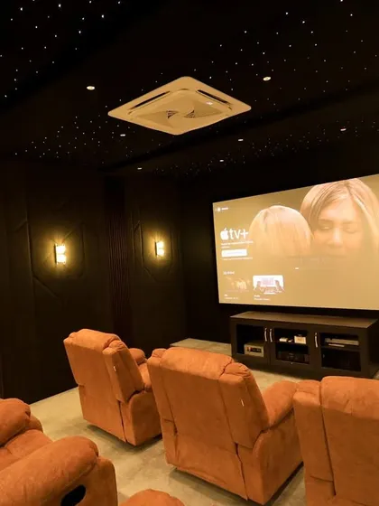 The large screen displays the Apple TV interface, ready for a night of entertainment. The warm lighting from the wall sconces creates a cozy and intimate atmosphere.